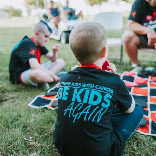 picture of a child at a free camp for kids with cancer with. the shirt says "Letting kids with cancer be kids again."